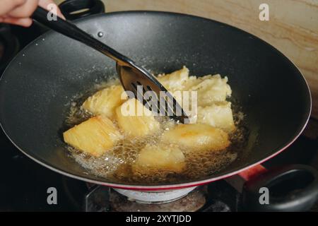 Eine Person brät Maniokscheiben in einer Pfanne. Die Maniokscheiben sind goldbraun und knusprig. Stockfoto