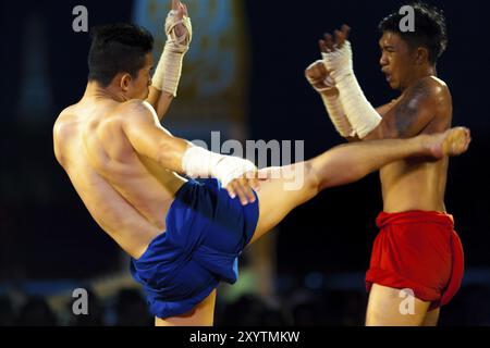 Bangkok, Thailand, 10. April 2007: Muay Thai Kickboxer mit gewickelten Händen tritt einen zuwinkenden Gegner während des traditionellen Kickboxspiels in der Ausstellung Stockfoto