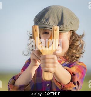 Lustiges Kind, das Holzschleuder vor blauem Sommerhimmel schießt Stockfoto