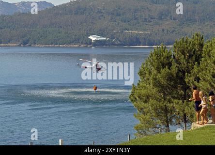 Die Brandbekämpfung Helikopter mit Bambi Warenkorb laden Wasser auf das Meer und die Gruppe von Menschen beobachten Stockfoto