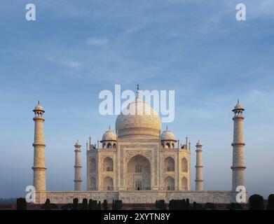 Ein wunderschönes Morgenorange an der vorderen Marmorfassade des ikonischen Taj Mahal, das sich unter einem ruhigen blauen Morgenhimmel aus Tele-Entfernung in Agra befindet. Stockfoto