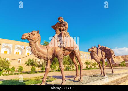 Skulpturengruppe einer Karawane mit Kamelen, die Güter entlang der Seidenstraße in der Nähe der alten Stadtmauern transportieren. Chiwa, Usbekistan - 16. Juli 2024. Stockfoto