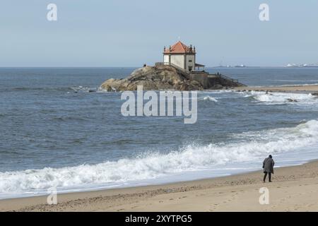 Spaziergänger am Sandstrand mit Surfen und Anblick Capela do Senhor da Pedra, historische Kapelle auf einem Felsen am Praia do Senhor da Pedra, Gulpilhares, Vila N Stockfoto