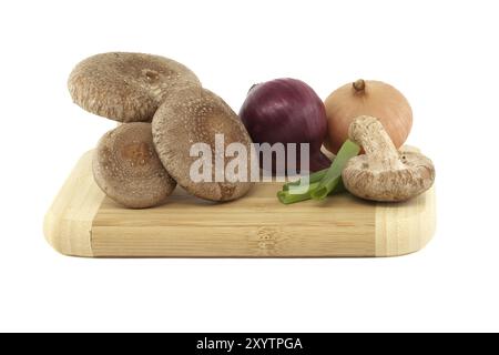 Shiitake-Pilze und verschiedene Zwiebelsorten auf einem Holzschneidbrett auf weißem Hintergrund. Rezepte und Heilkräuter Stockfoto