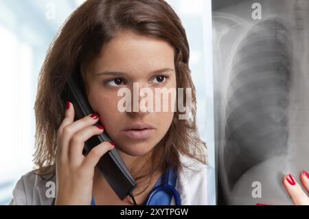 Junge Ärztin untersucht eine Röntgenaufnahme während des Gesprächs am Telefon Stockfoto