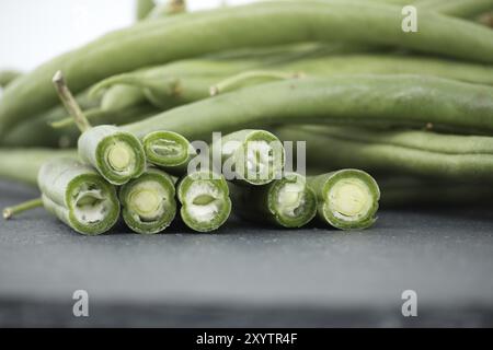 Ein Haufen geschnittener grüner Bohnen auf einem Tisch aus schwarzem Stein auf weißem Hintergrund. Bio- und Diätkost Stockfoto