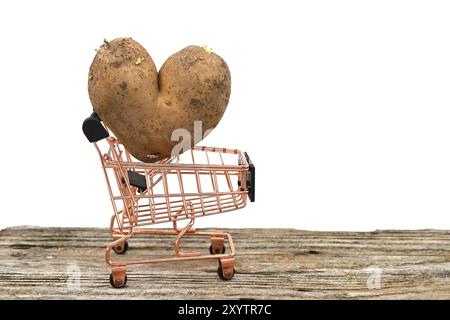 Herzförmige Kartoffel gegen einen Einkaufswagen auf verwittertem Holztisch über einem weißen Stockfoto