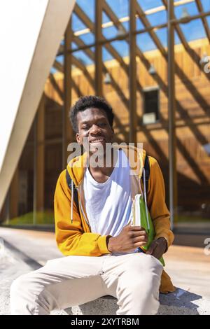 Vertikales Porträt mit Kopierraum eines glücklichen afroamerikaners, der vor der Universität sitzt Stockfoto