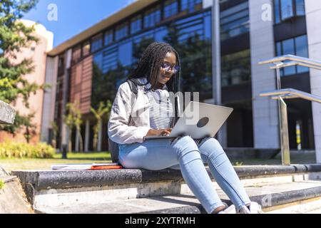 Fokussierte afrikanische Studentin mit Laptop auf Außentreppen auf dem Campus Stockfoto