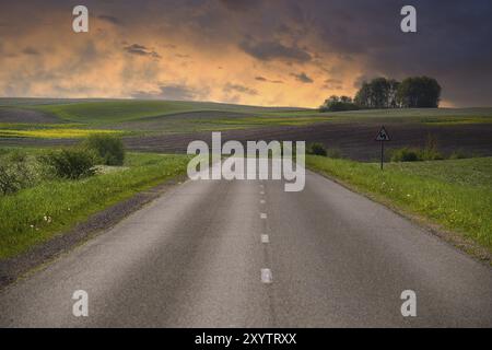 Leere zweispurige Asphaltstraße, die durch eine ruhige und offene Landschaft führt. Rund um die Straße gibt es grasbewachsene Ebenen und kleine Hügel Stockfoto