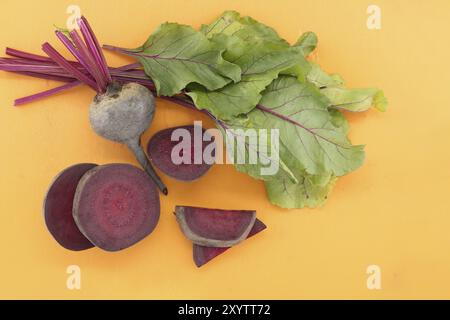 In Scheiben geschnittene und ganze frische Bio-Rote Bete mit grünen Blättern auf gelbem Schneidebrett, Draufsicht mit kostenlosem Platz für Kopien Stockfoto