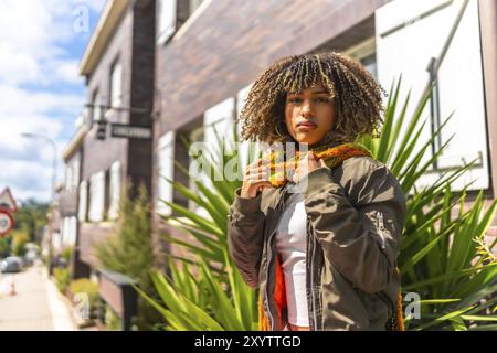 Lateinische Frau in warmen Kleidern, die an einem sonnigen Tag vor einem Haus auf der Straße steht Stockfoto