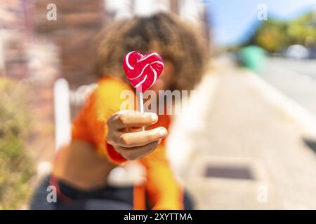 Konzentrieren Sie sich auf die Hand einer jungen lateinfrau, die auf der Straße einen herzförmigen Lutscher hält Stockfoto