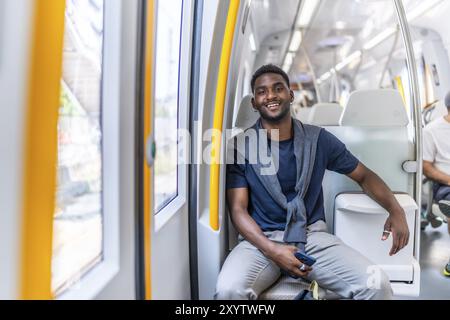Porträt eines gutaussehenden jungen afrikanischen Mannes, der in die Kamera lächelt, während er in der öffentlichen U-Bahn sitzt und pendelt Stockfoto