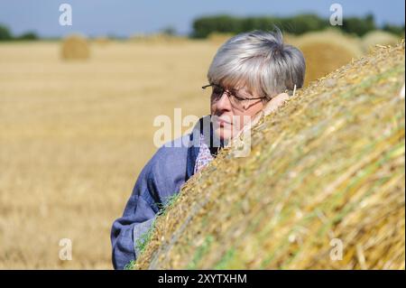 Die grauhaarige Dame lehnt ihren Kopf gegen einen Strohballen und ruht Stockfoto