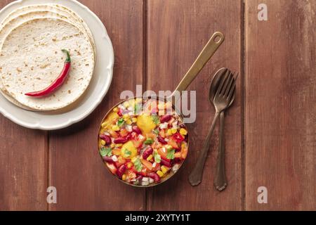 Huevos Rancheros, mexikanische Spiegeleier, von oben geschossen mit Pico de gallo Salat, Tortillas und einer roten heißen Chili-Pfeffer auf einem dunklen rustikalen Holzbackgr Stockfoto