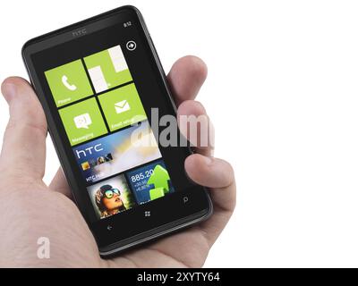 Hand mit einem Windows 7-Telefon. HTC HD7 Smartphone mit Desktop-Kacheln auf dem Display isoliert mit Beschneidungspfad auf weißem Hintergrund. Hochwertige Fotos Stockfoto