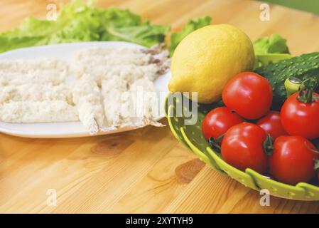 Rohe Garnelen in Teig, bereit zum Rösten, neben einem Korb Gurken, Zitronengurken und Tomaten vor dem Hintergrund von Salatblättern auf einem Holz Stockfoto