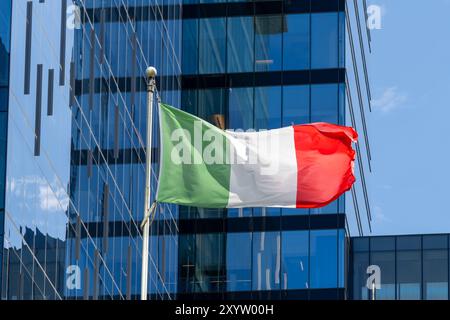 Eine italienische Nationalflagge, die im Wind winkt, mit einem Glasgebäude im Hintergrund. Stockfoto