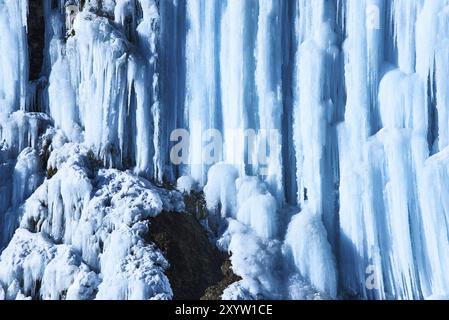 Große Eiszapfen hängen an der Klippe des Flussufers. Blauer Hintergrund Stockfoto