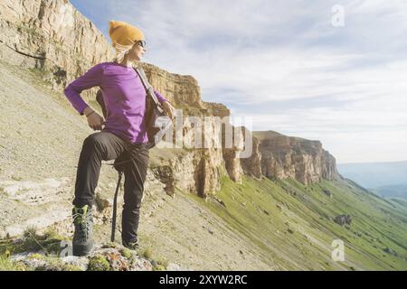 Ein Mädchen mit Sonnenbrille legt einen Rucksack auf die Natur vor einem Hintergrund epischer Felsen, die sich auf eine Wanderung mit Klettern vorbereiten Stockfoto