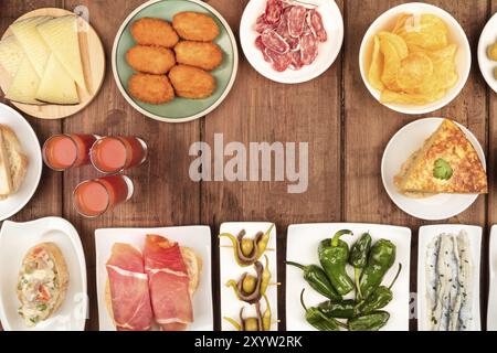Spanische Tapas, eine Auswahl an Snacks, Top-Shot. Gazpacho, Tortilla, Marmelade, Käse usw., von oben auf einem dunklen rustikalen Holzhintergrund mit einem Platz Stockfoto