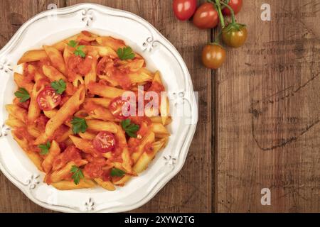 Ein Foto von einem Teller Pasta mit Tomatensauce. Penne Rigate mit Cherry Tomaten und frische Petersilie, auf einem dunklen rustikalen Textur mit einem p Stockfoto