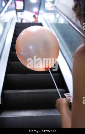 Frau mit einem Ballon liest eine Anzeige, während sie auf einer Rolltreppe in einem Einkaufszentrum steht Holiday Shopping Konzept Stockfoto