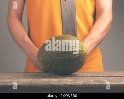 Junger Mann mit einem alten Cleaver und eine frische Melone auf eine rustikale Küche Tabelle Stockfoto