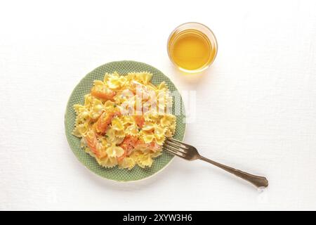 Ein Teller mit Lachsnudeln. Farfalle mit Räucherlachs und Sahnesauce, von oben auf einer weißen Tischdecke mit einem Glas Wein und einem Platz für Tex Stockfoto