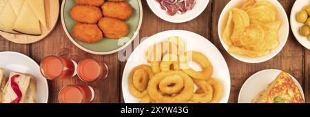 Ein Panorama spanischer Tapas, ein Foto von einer Auswahl an Snacks über dem Kopf. Gazpacho, Tintenfischringe, Tortilla, Käse usw., von oben auf einem dunklen rustikalen W Stockfoto