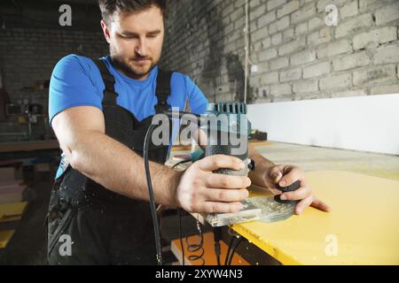 Der professionelle Zimmermann verarbeitet die Kunststoffkanten der Arbeitsplatte mit einem speziellen Elektrowerkzeug Stockfoto