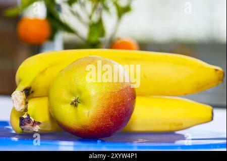2 reife Bananen und ein Apfel liegen auf dem Tisch vor dem Küchenfenster Stockfoto