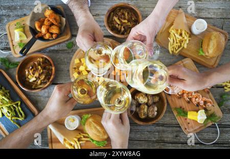 Hände mit weißen Wein Toasten über serviert Tisch mit Essen. Freundschaft und Glück Konzept Stockfoto