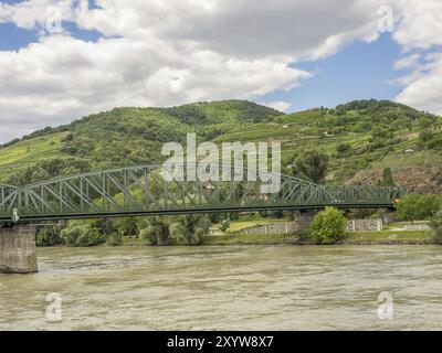 Metallbrücke über einen Fluss mit grünen Hügeln und bewölktem Himmel im Hintergrund, Duernstein, Wachau, Donau, Österreich, Europa Stockfoto