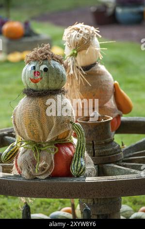 Zwei Kürbisfiguren auf einem Wagenrad, kunstvoll mit Stroh und Sack verziert, herbstliche Gartenlandschaft im Hintergrund, borken, münsterland, Stockfoto