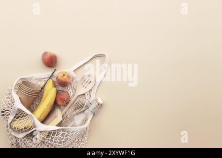 Umweltfreundliche Sommer konzeptionelle Wohnung lag auf beigem Hintergrund mit Öko Einkaufstasche, Küche Recycling Besteck, Glasflasche Wasser, Bananen und Apfel Stockfoto