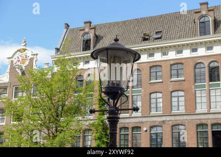 Eine altmodische Straßenlaterne vor einem historischen Gebäude mit vielen Fenstern und Oberlichtern unter blauem Himmel, Amsterdam, Niederlande Stockfoto