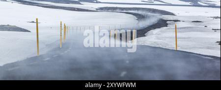 Eine Nebelspur zieht sich über eine gekrümmte Asphaltstraße durch eine verschneite Landschaft Stockfoto