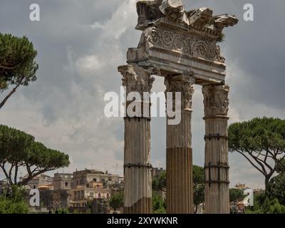 Drei antike Säulen mit verzierten Kapitellen vor bewölktem Himmel und urbanem Hintergrund, Rom, Italien, Europa Stockfoto