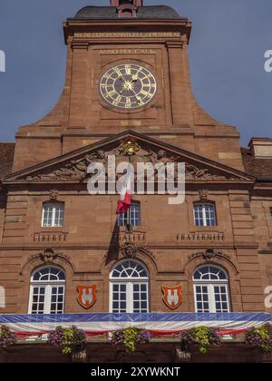 Historisches Gebäude mit großem Turm und Uhr, französischer Flagge und der Inschrift „Liberte, Egalite, Fraternite“ unter klarem blauem Himmel, Weissenburg, ALSA Stockfoto