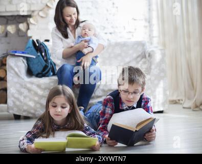 Sohn und Tochter mit Mutter und Bruder, die auf dem Sofa sitzen. Kinder lesen Bücher im Wohnzimmer. Fokus auf die Kinder Stockfoto