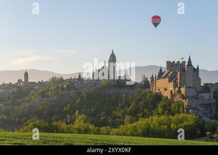 Wunderschöner Blick auf ein Schloss bei Sonnenaufgang mit einem Heißluftballon am Himmel und grünen Feldern im Vordergrund, Kirche, Iglesia San Esteban, Kathedrale, Al Stockfoto