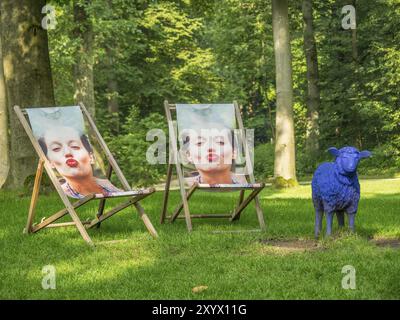 Zwei Stühle mit Frauenporträts und einem lila Schaf auf einer Wiese im Wald, Bad Lippspringe, Deutschland, Europa Stockfoto