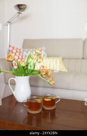 Schöne orange Tulpen Bukett mit zwei Tassen Tee auf Holztisch im Wohnzimmer Stockfoto