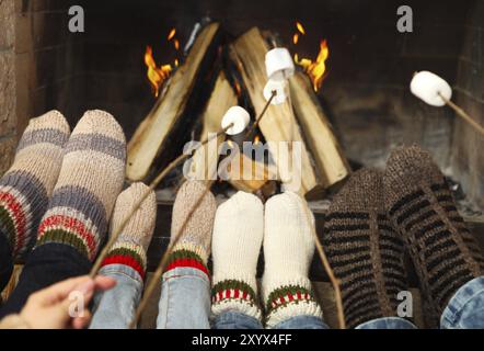 Füße von der Familie Erwärmung bei einem Kamin mit Marshmallows auf sticks Stockfoto