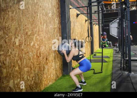 Chinesisch-Fit-Frau trainiert mit Medizinball im Fitnessstudio, hockt und wirft den Ball auf Stockfoto