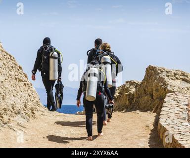 Eine Gruppe von Tauchern mit Tauchausrüstung geht zum Meer vor dem blauen Himmel und den Wolken in Ägypten Dahab Stockfoto