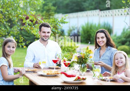 Glückliche Familie von vier Personen, die Mahlzeit zusammen, während am Esstisch im Freien sitzen Stockfoto