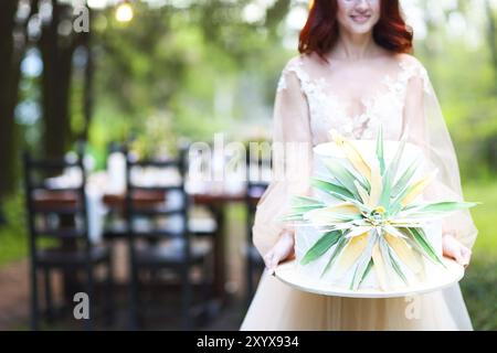 Wunderschöne Hochzeitstorte mit Blume in der Hand der Braut, im Freien Stockfoto